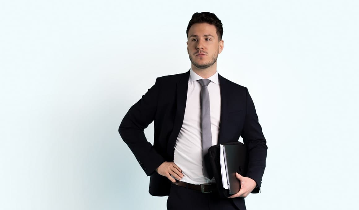 Ein Mann im Business-Anzug hält eine Aktentasche unter seinem linken Arm.