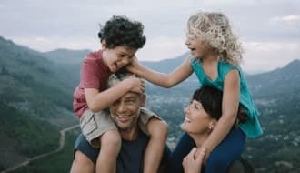 Ein Mann und eine Frau mit je einem Kind auf den Schultern lachen vergnügt.