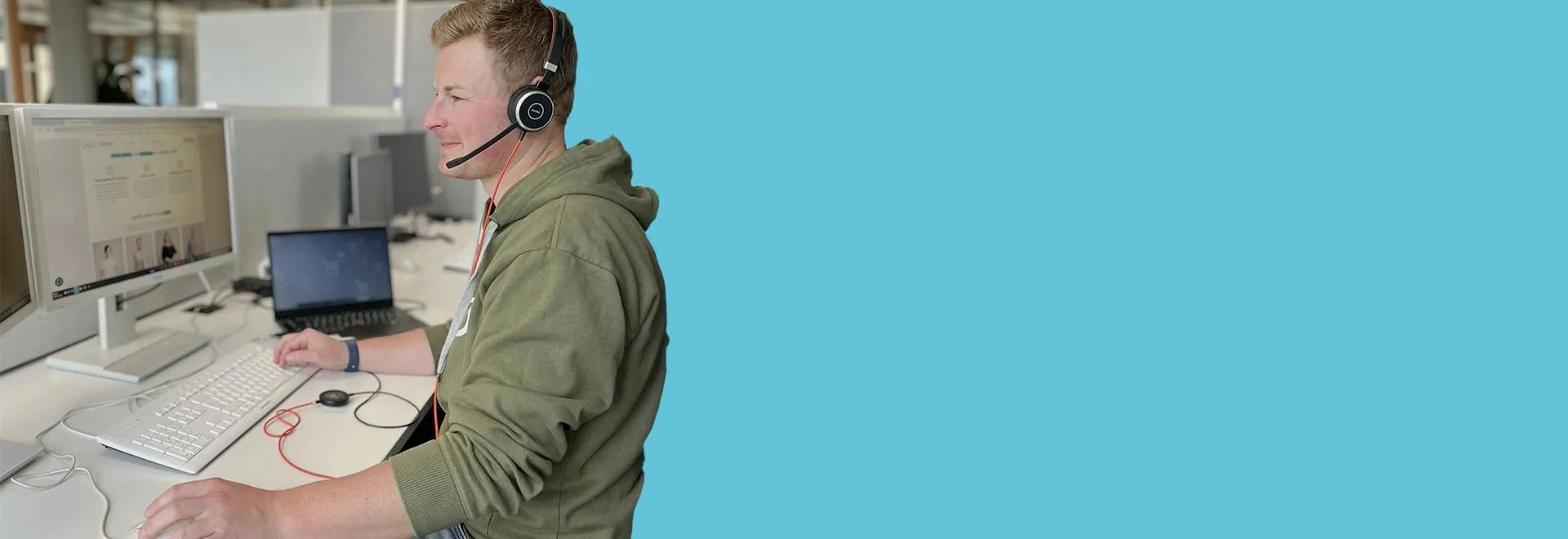 Moritz sitzt an seinem Lieblingsschreibtisch im Office und telefoniert per Headset mit Kollege.