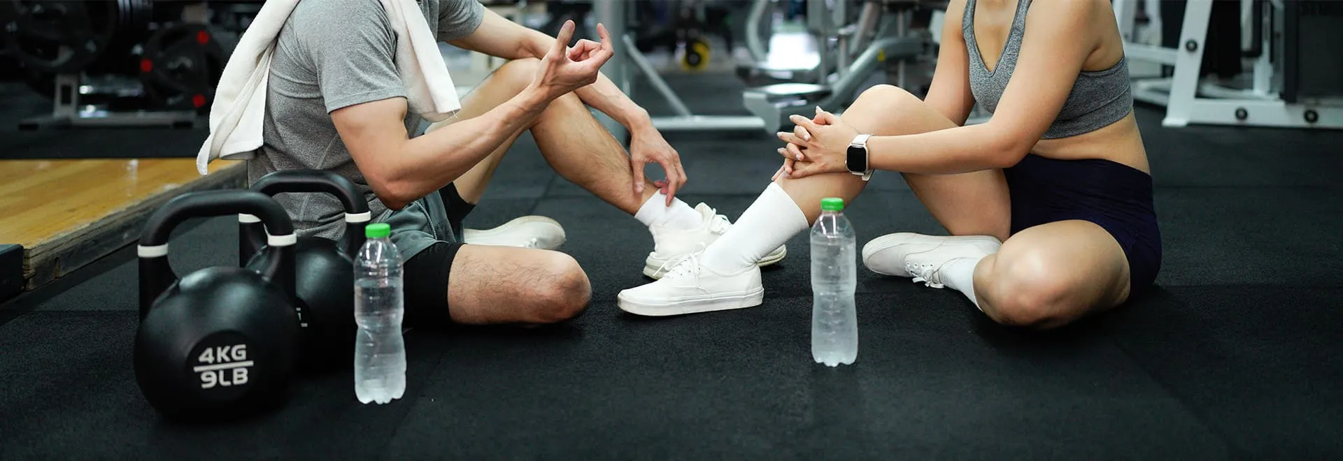 Unfallversicherung Sport: Zwei Personen sitzen im Gym auf Sportmatten und unterhalten sich.