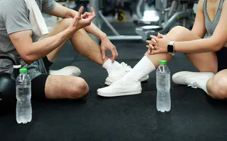 Unfallversicherung Sport: Zwei Personen sitzen im Gym auf Sportmatten und unterhalten sich.