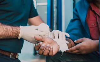 Ein Arbeitsunfall kann in jedem Job passieren: Ein Sanitäter verbindet einem Mann die rechte Hand.