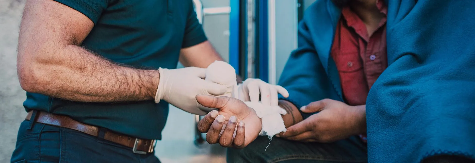 Ein Arbeitsunfall kann in jedem Job passieren: Ein Sanitäter verbindet einem Mann die rechte Hand.