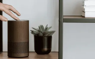 Smart-Home-Sicherheit: Eine Hand greift nach einem Smart-Speaker, der auf einem Bücherregal steht.