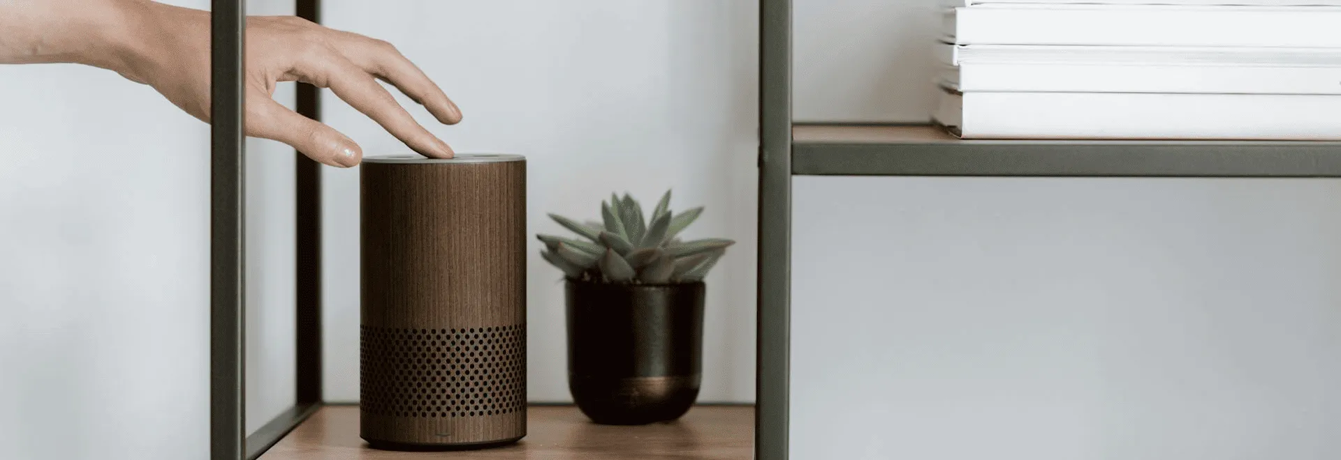 Smart-Home-Sicherheit: Eine Hand greift nach einem Smart-Speaker, der auf einem Bücherregal steht.