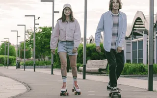 Für Aktive lohnt sich eine Unfallversicherung häufig: eine Rollerskaterin und ein Skateboarder fahren auf einer asphaltierten Promenade.