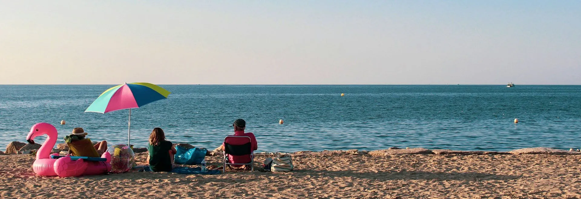 Eine Familie sitzt am Strand mit Sonnenschirm und aufblasbarem Flamingo.