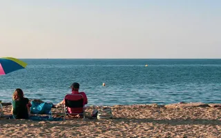 Eine Familie sitzt am Strand mit Sonnenschirm und aufblasbarem Flamingo.