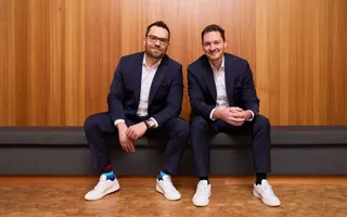 Julian Grauer (l) und Sven Tippelt (r) sitzen auf einer Bank im Campus der W&W-Gruppe.