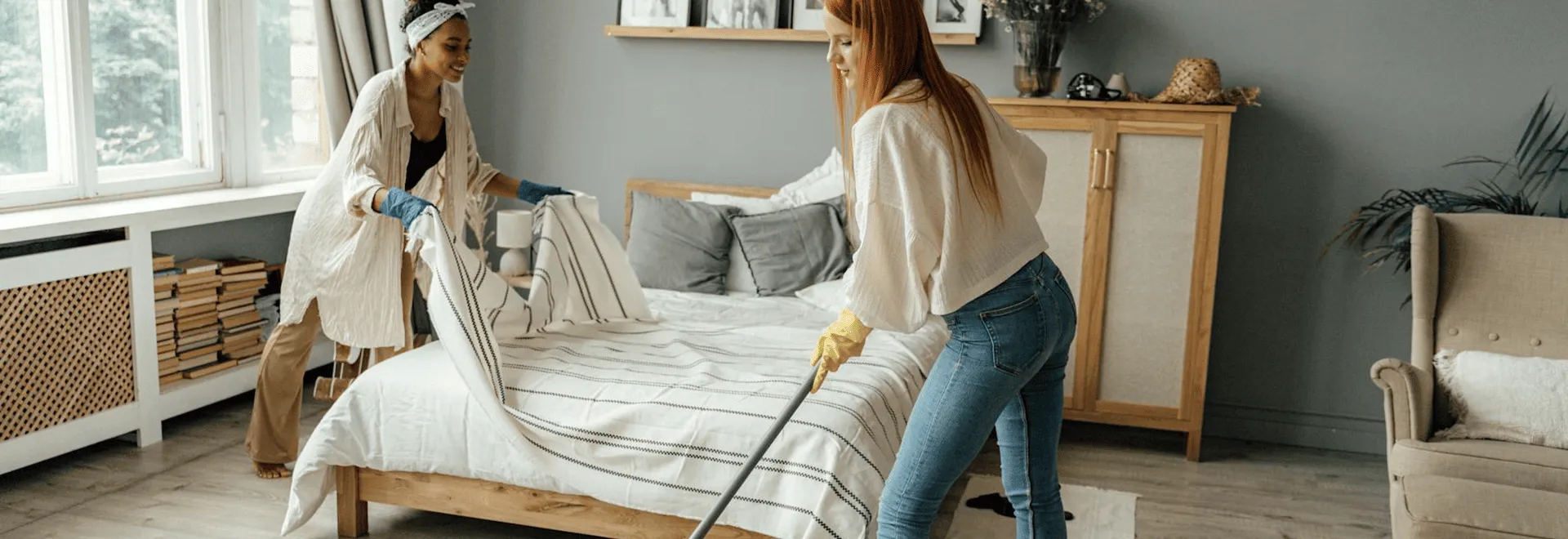 Beim Tema Frühjahrsputz können viele Hände helfen: Zwei Freundinnen putzen ein Schlafzimmer.