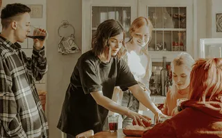 Eine Hausparty: Sechs Menschen sitzen zusammen am Küchentisch und trinken Rotwein/Traubensaft. Wird mit dem Wein gekleckert, kann eine Haftpflichtversicherung bei Mietsachschäden helfen!