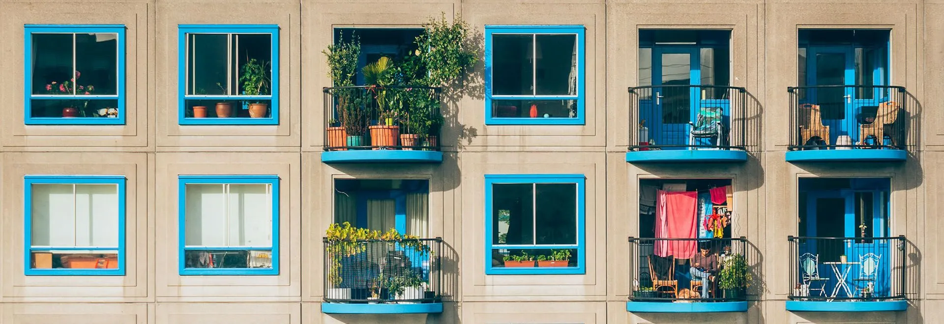 Urlaub auf Balkonien kann echt schön sein: Ein Haus mit blauen Fenstern und begrünten Balkonen in der Sonne.