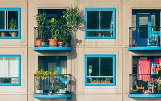 Urlaub auf Balkonien kann echt schön sein: Ein Haus mit blauen Fenstern und begrünten Balkonen in der Sonne.