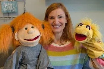 Eine Handpuppenspielerin im bunt gestreiften Pulli mit zwei Handpuppen