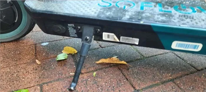 Nahaufnahme eines E-Scooters, bei dem man nur einen Teil der Standfläche mit Ständer und ein halbes Vorderrad erkennen kann