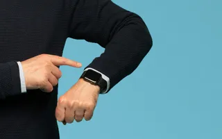 Person zeigt mit dem Finger auf Armbanduhr am Handgelenk