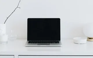 Ein aufgeklappter Laptop auf einem aufgeräumten, weißen Schreibtisch.