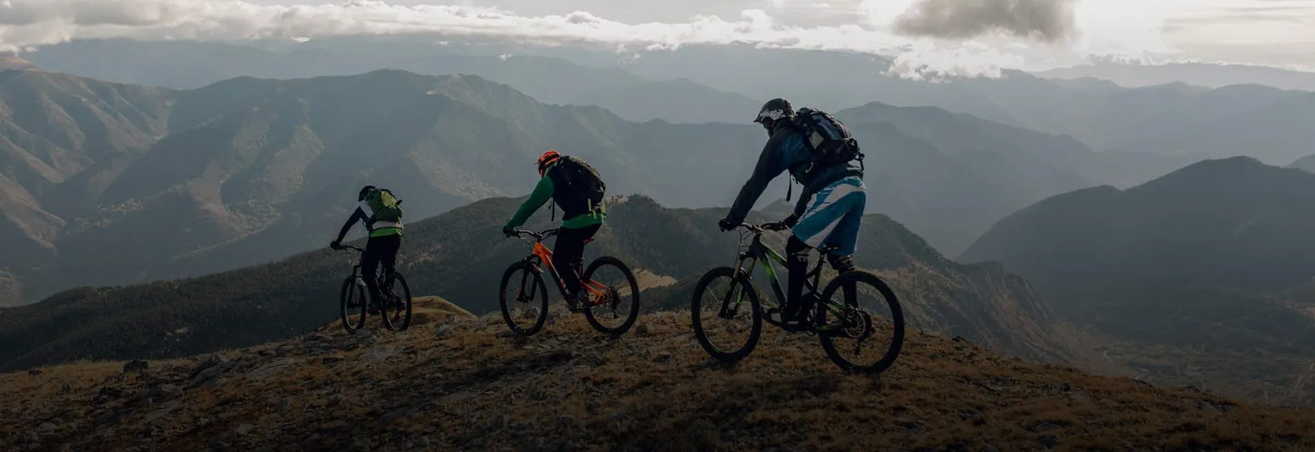Drei Personen fahren Mountainbike im Gebirge. Für viele Sportarten eignet sich die Adam Riese Unfallversicherung.
