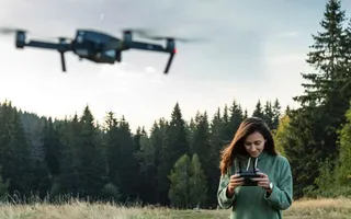 Frau steuert Drohne auf einer großen Wiese vor Wald