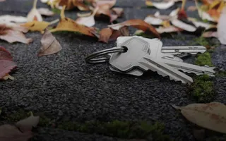 Ein verlorener Schlüsselbund liegt auf einem gepflasterten Boden mit bunten Laubblättern. 