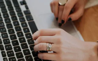 Person mit Smartwatch und Ringen tippt auf ihrem Macbook